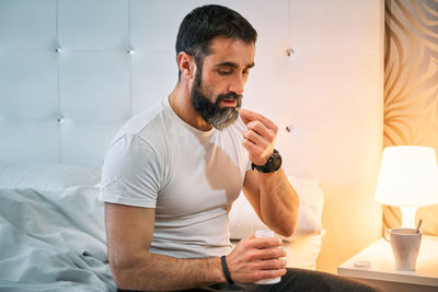 Person with some kind of problem sitting on the bed and taking a pill