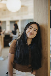 Portrait of smiling young female student leaning on wall