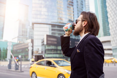 Side view of a man drinking from car in city