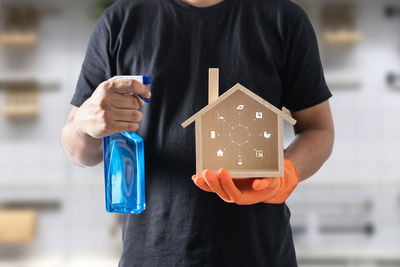 Midsection of man holding spray bottle and model house