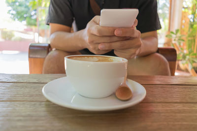 Close-up of man holding coffee while sitting on table