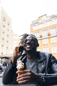 Smiling man with ice cream talking on smart phone in sidewalk cafe