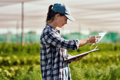 Side view of young woman examining documents at farm