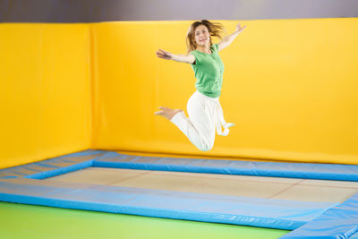 Full length of a woman jumping against yellow wall