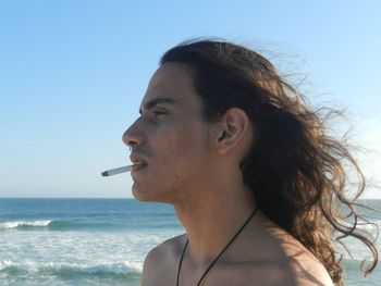 Portrait of young woman looking away at beach against sky