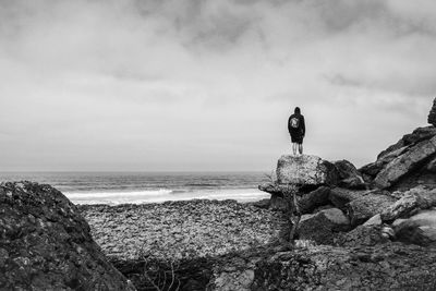 Rear view of man standing on rock by sea against sky