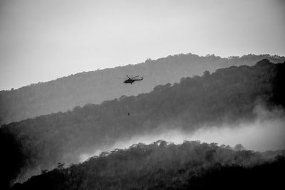 Silhouette of airplane flying over mountains against sky