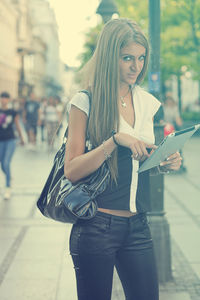 Portrait of young woman using digital tablet while standing on city street