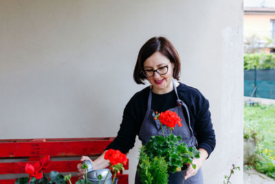 Dark haired woman standing with geranium flower pot in her hands