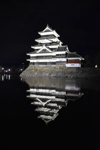 Illuminated building by lake against sky at night