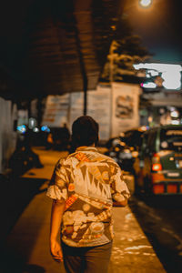 Rear view of man standing on street at night