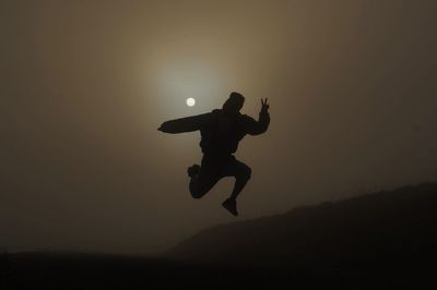 Silhouette man jumping over field against sky at dusk