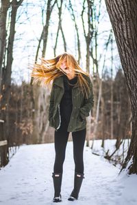 Full length of woman standing on tree trunk during winter