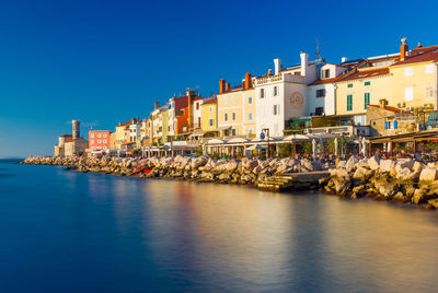 Buildings by sea against clear blue sky