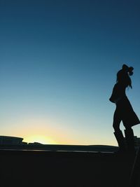 Silhouette woman standing on roof against clear sky