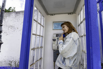 Smiling woman talking on telephone standing in telephone booth