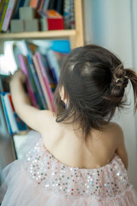 Rear view of girl by bookshelf at home