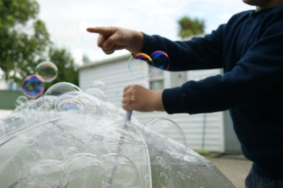 Midsection of boy touching bubbles on umbrella against sky