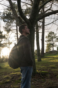 Man standing by tree trunk in forest