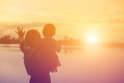 Woman standing with arms outstretched against sky during sunset