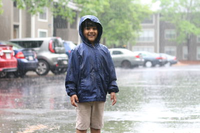 Portrait of smiling boy standing on wet city street during rainy season