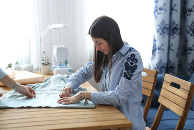 Girl works in a home sewing workshop, pins the pattern to the blue fabric.