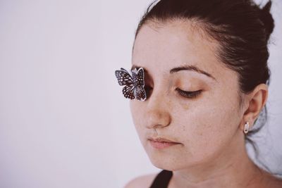 Close-up of young woman with artificial butterfly on eye against white background