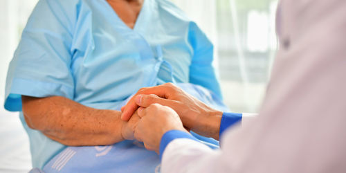 Cropped image of male doctor holding hands with female patient in hospital