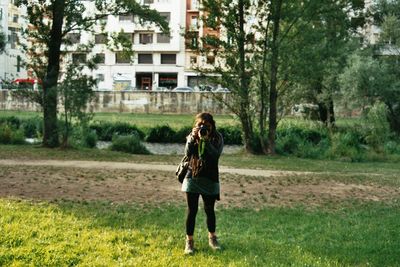 Full length of teenage girl photographing while standing on grassland