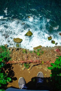 Low section of person standing on rock by sea