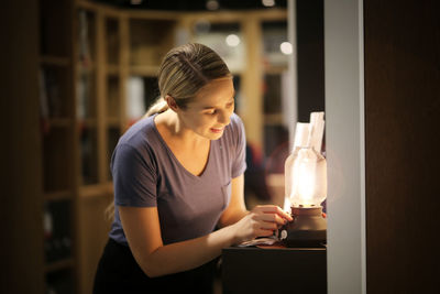 Smiling woman adjusting flame of oil lamp at home