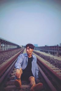 Man sitting on railroad track against sky