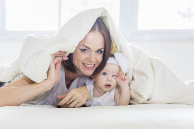 Portrait of mother and daughter lying on bed under blanket