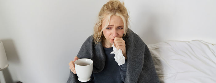 Young woman drinking coffee while sitting on bed at home