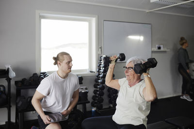 Woman exercising with dumbbell with trainer checking his progress