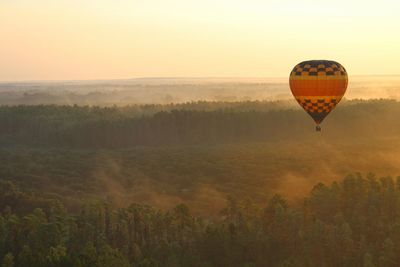 Hot air balloon flying over field against sky during sunset