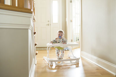Portrait of cute toddler sucking pacifier while standing in baby walker at home