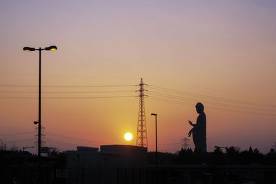 Silhouette man and electricity pylon against sky during sunset