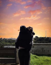 Rear view of woman standing against sky during sunset