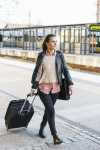 Full length of businesswoman pulling wheeled luggage while walking on railroad station platform