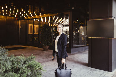 Portrait of female entrepreneur with bag standing at building entrance