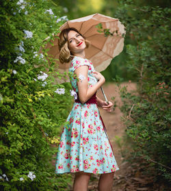 Young woman with umbrella standing against trees