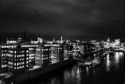 Illuminated buildings by river against sky at night