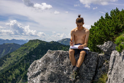 Full length of shirtless man standing on rock against sky