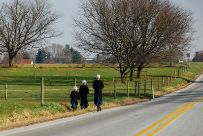 Rear view of amish women walking on road amidst bare trees