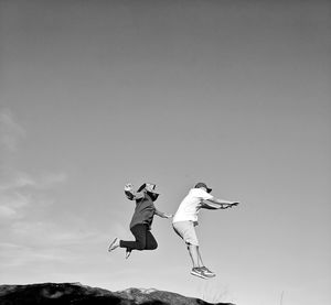 Low angle view of people jumping against sky