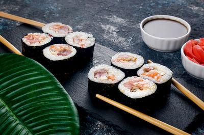 Fresh tasty sushi with salmon in wooden chopsticks on a dark background. 