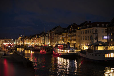 Sailboats moored on river by illuminated buildings in city at night