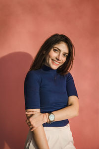 Portrait of smiling young woman standing against wall