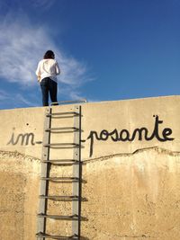 Low angle view of text on wall with man standing against blue sky